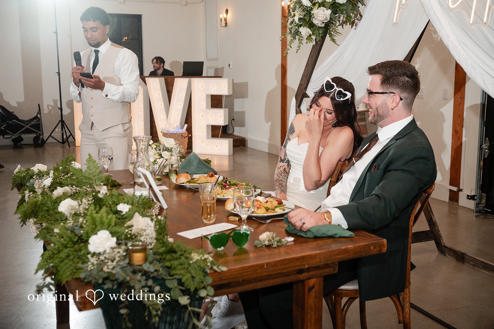 Noah + Jade bride and groom sitting at their decorated head table during wedding speeches.
