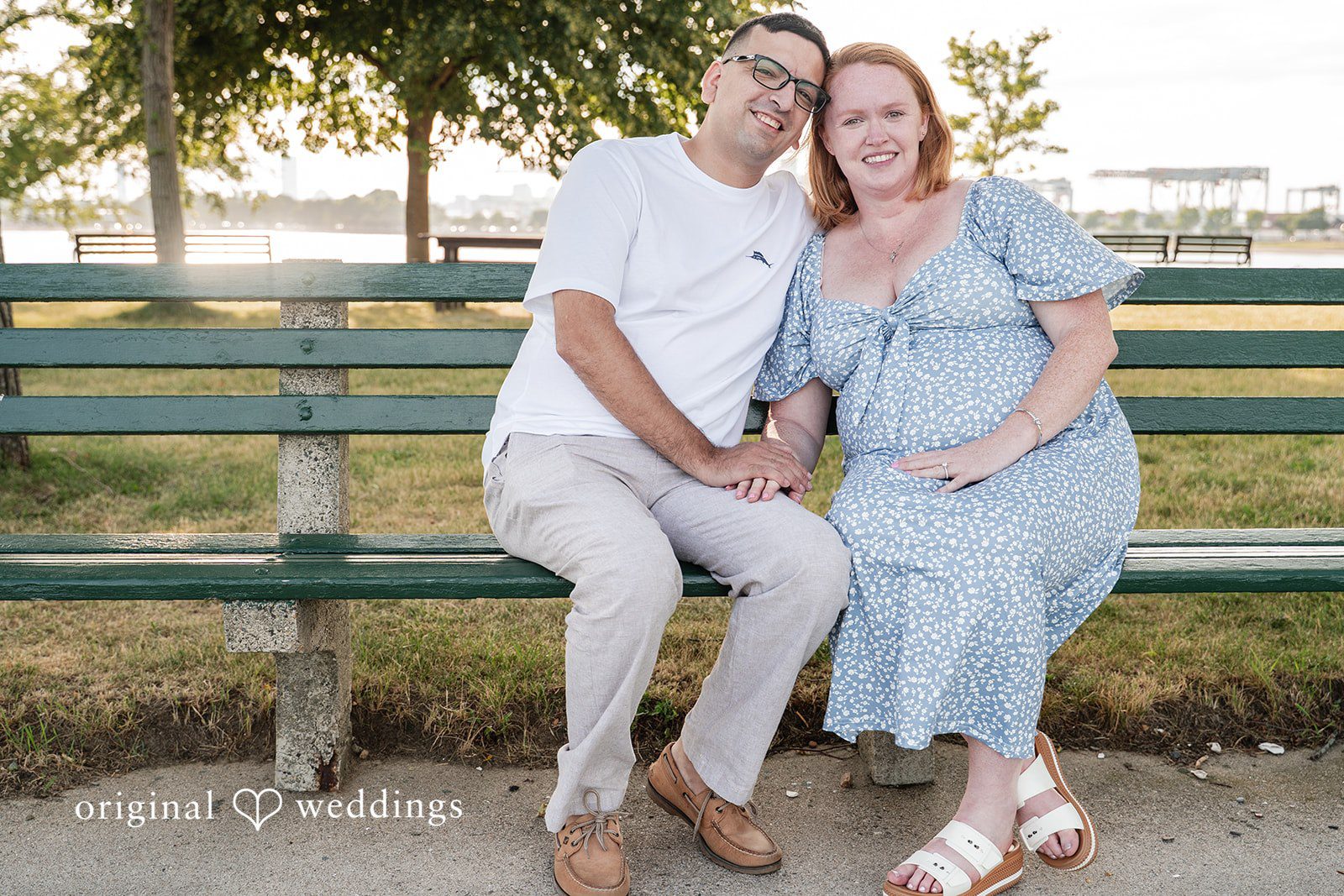 Kelly + Geoffrey A couple sitting closely together on a green park bench, smiling warmly during their Photo session.