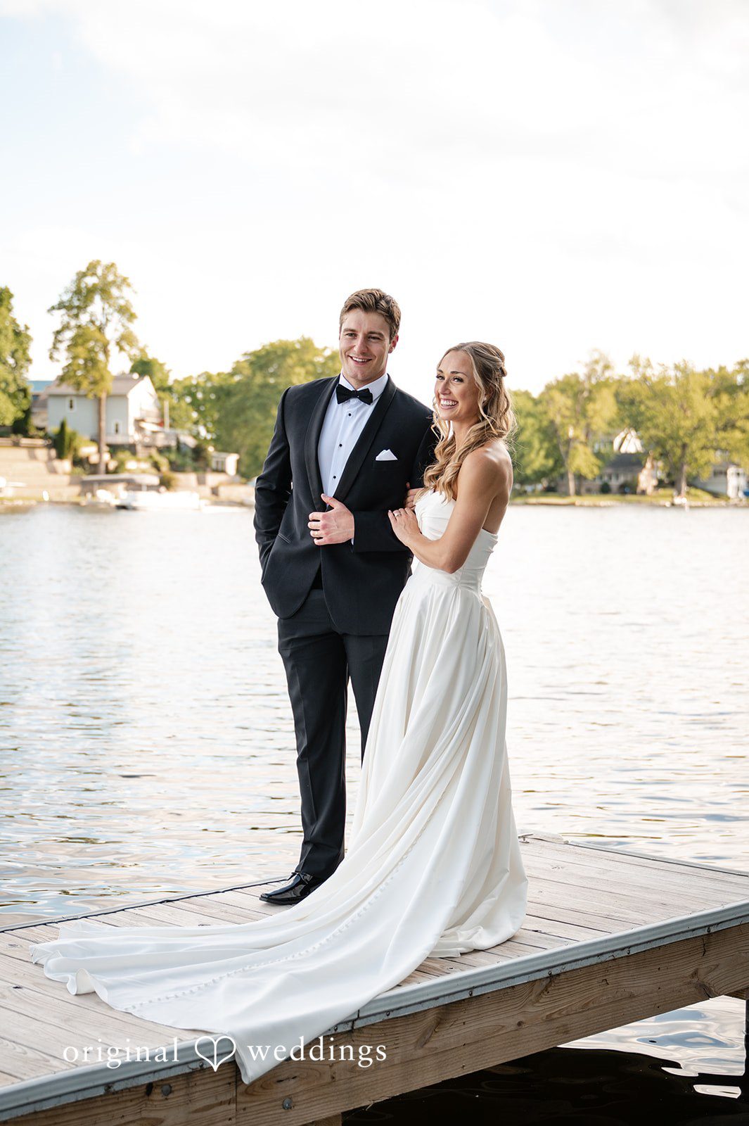 Brandi + Ryan Bride and groom standing together on a lakeside dock during sunset