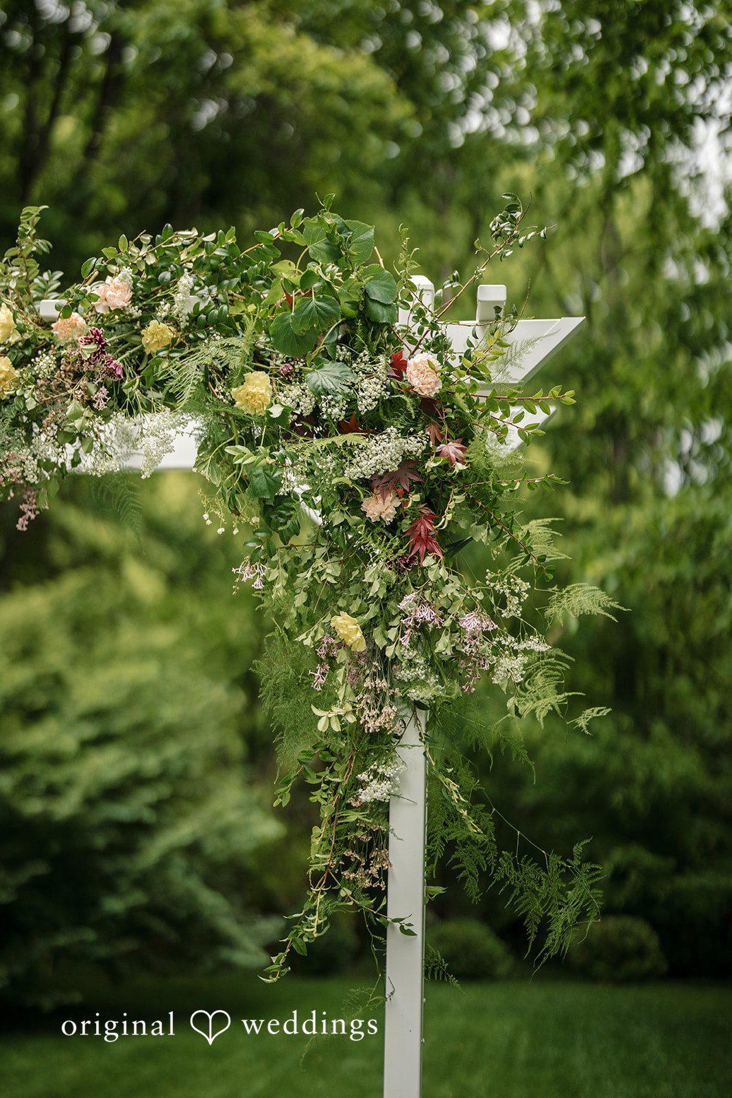 Meghan + Rowan A close-up view of a rustic wooden wedding arch decorated with vibrant flowers and green leaves.