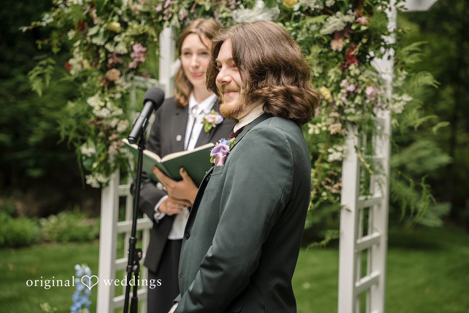 Meghan + Rowan A groom smiling during the wedding ceremony while standing next to an officiant holding a book.