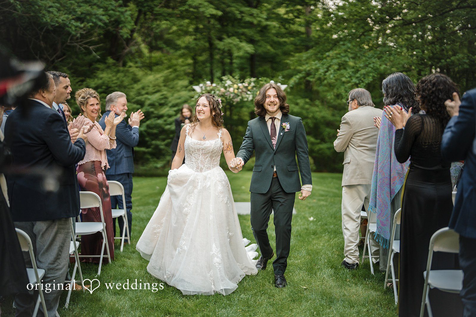 Meghan + Rowan A newly married bride and groom smiling as they walk down the aisle together while guests applaud.