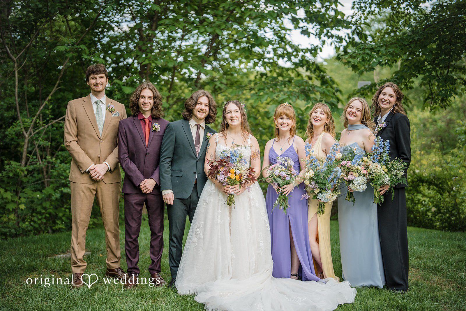 Meghan + Rowan A full wedding party poses together on a lawn, featuring the bride, groom, bridesmaids, and groomsmen.
