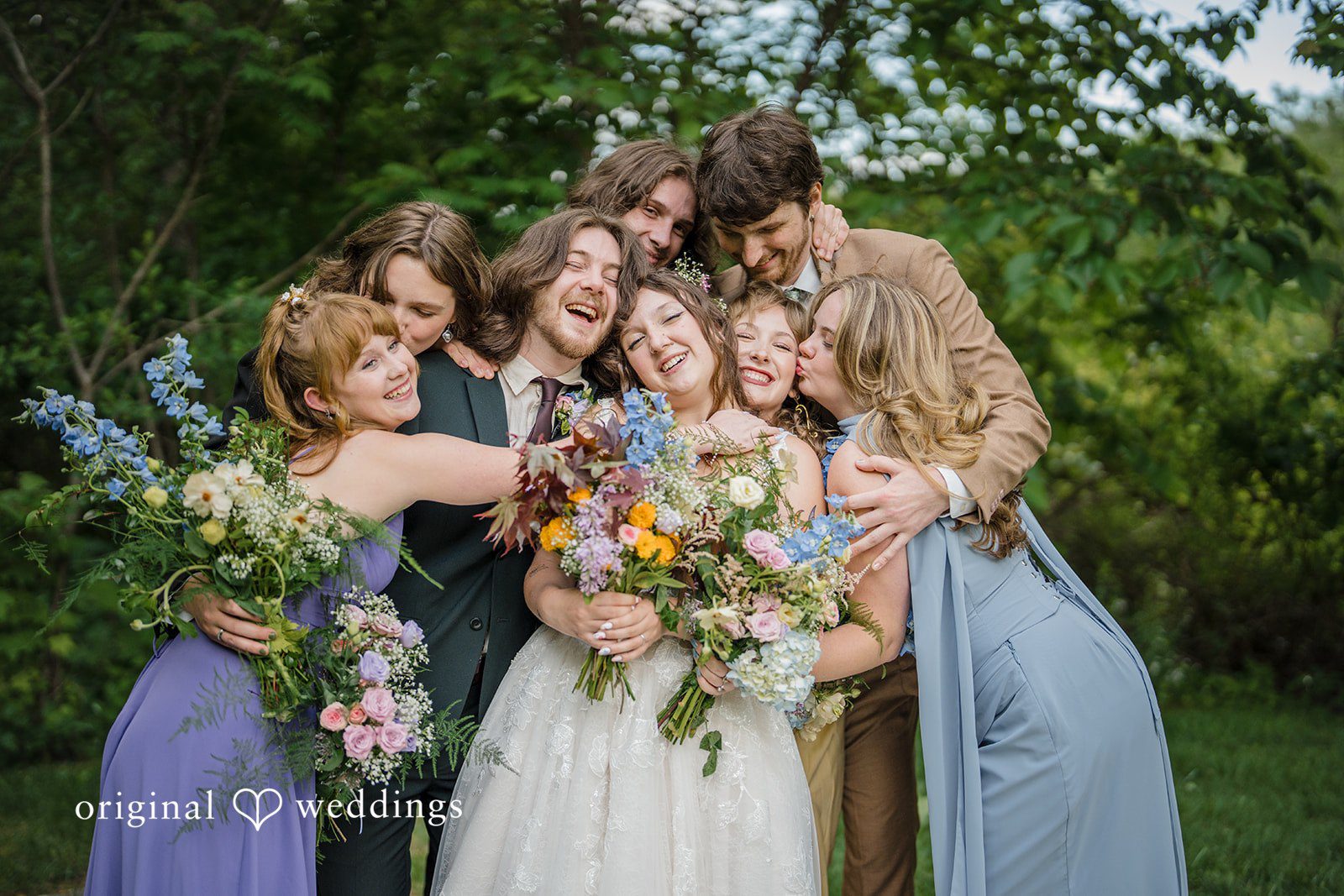 Meghan + Rowan A wedding party gathers tightly together for a joyful group hug on a lawn.