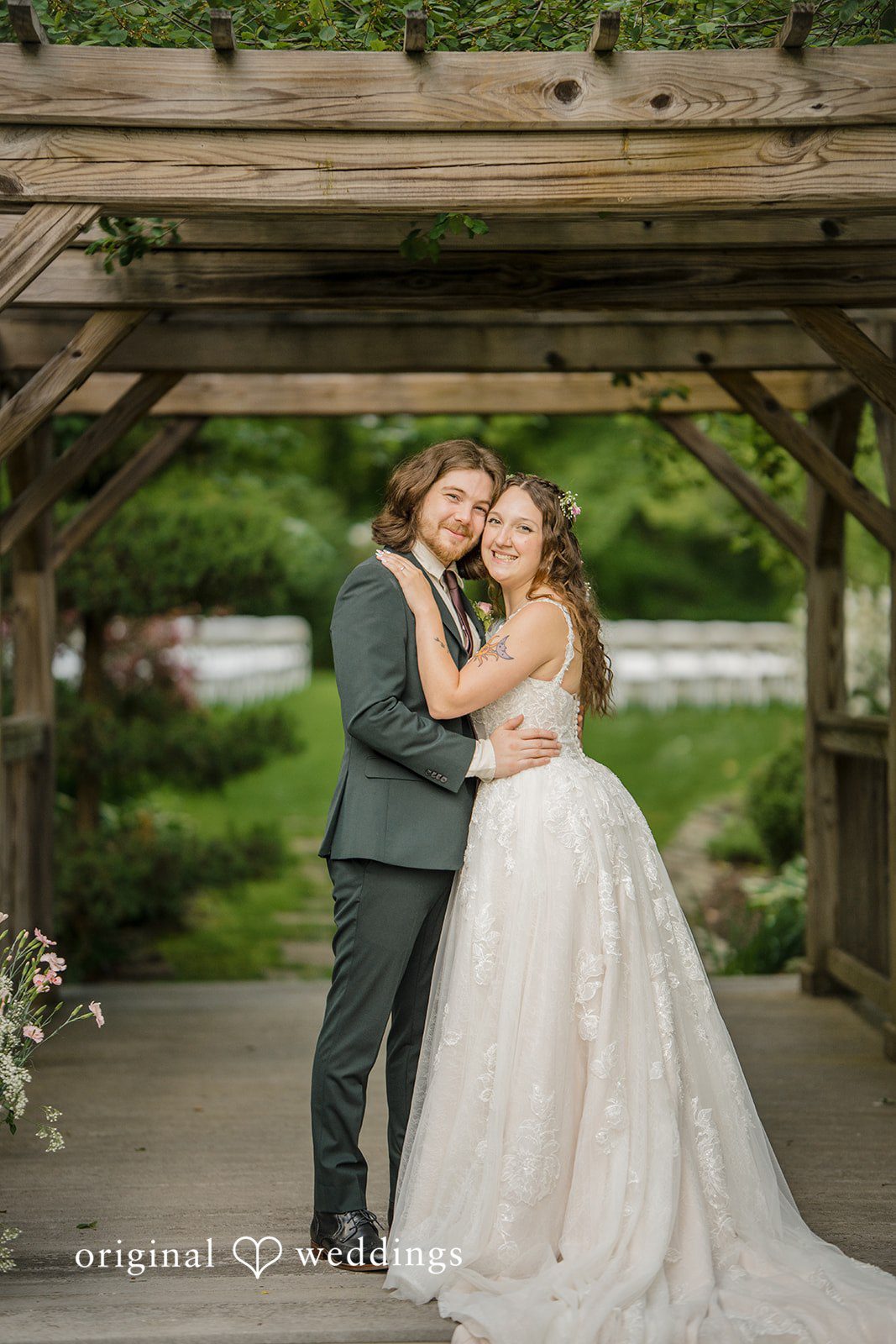 Meghan + Rowan A bride and groom smiling and embracing while posing under a wooden pergola walkway.