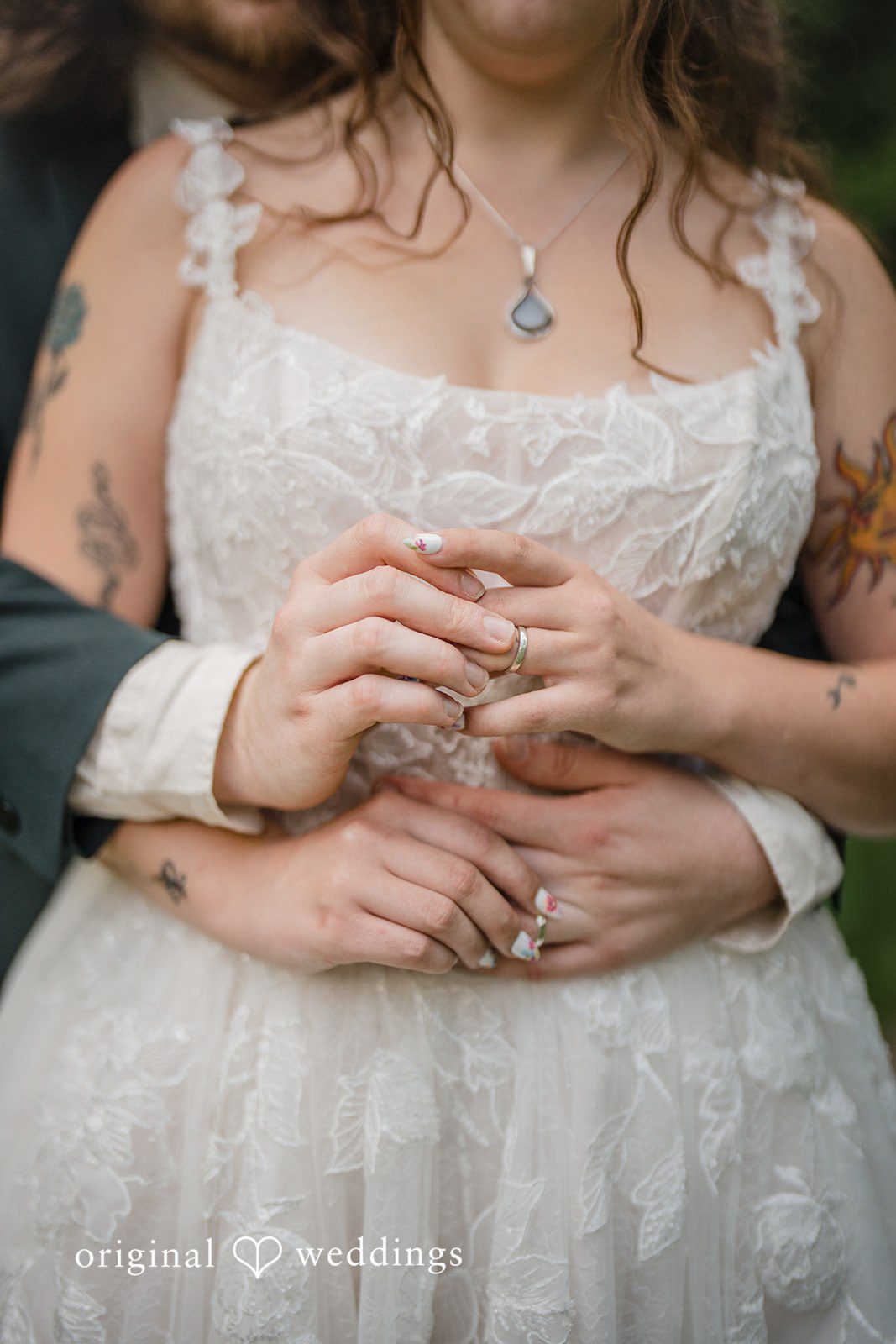 Meghan + Rowan A close-up view of a groom's hands gently wrapping around a bride's waist over her white lace gown.