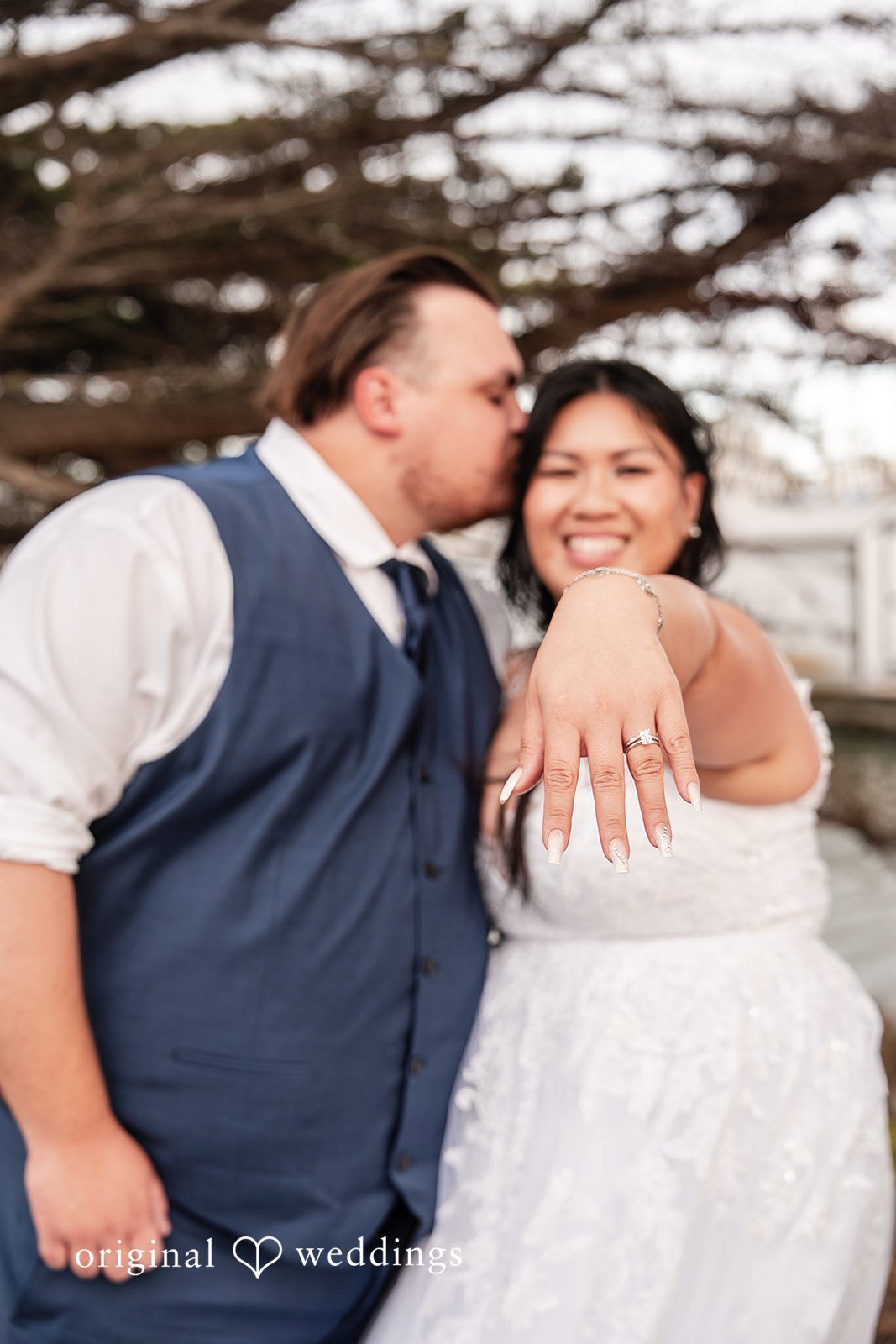 Thuy + Ryan Close-up of wedding rings while Groom kissing bride her forehead at Double Tree by Hilton Hotel Berkeley
