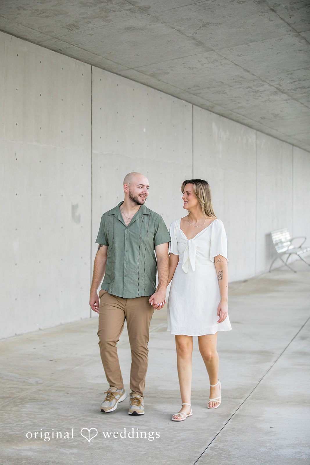 Lauren + Miles A couple walking hand-in-hand past a concrete wall.