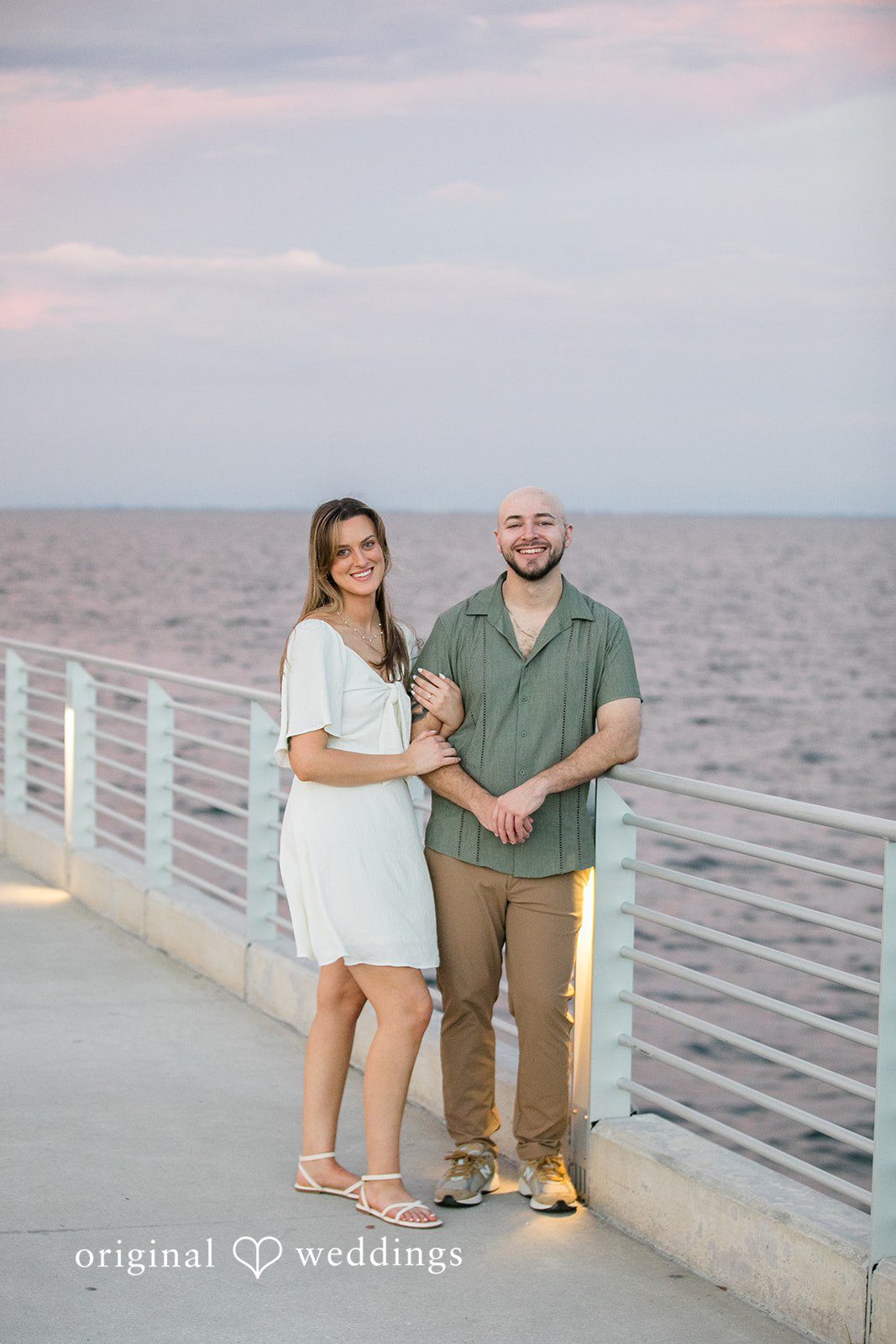 Lauren + Miles A couple standing together next to a railing with open water behind them.