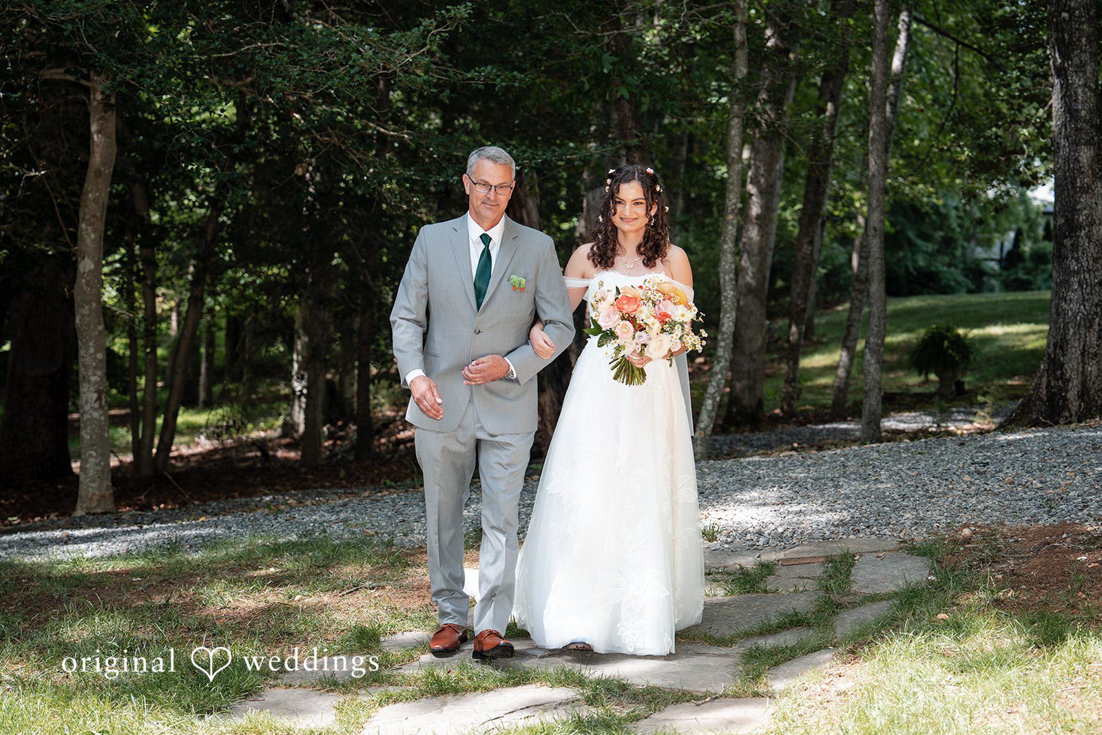 Conner + Ashley A bride and groom walking together down a paved forest path.