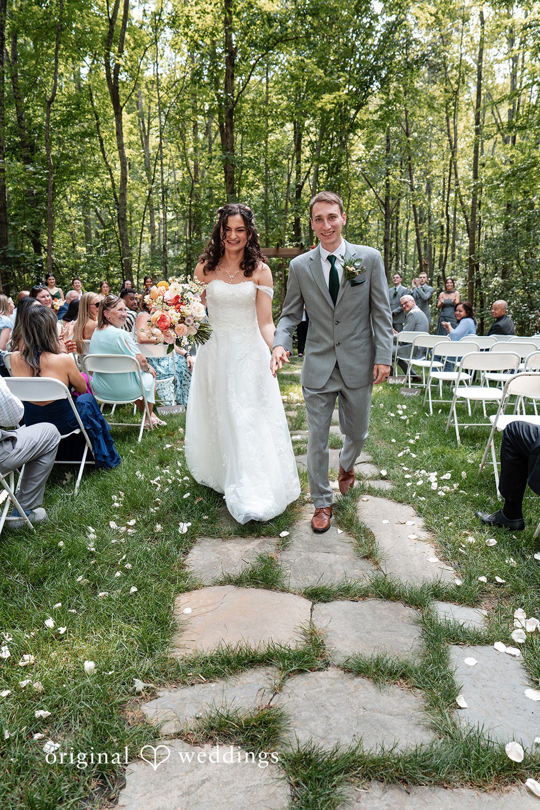Conner + Ashley A newlywed couple walking down a stone path as guests look on.