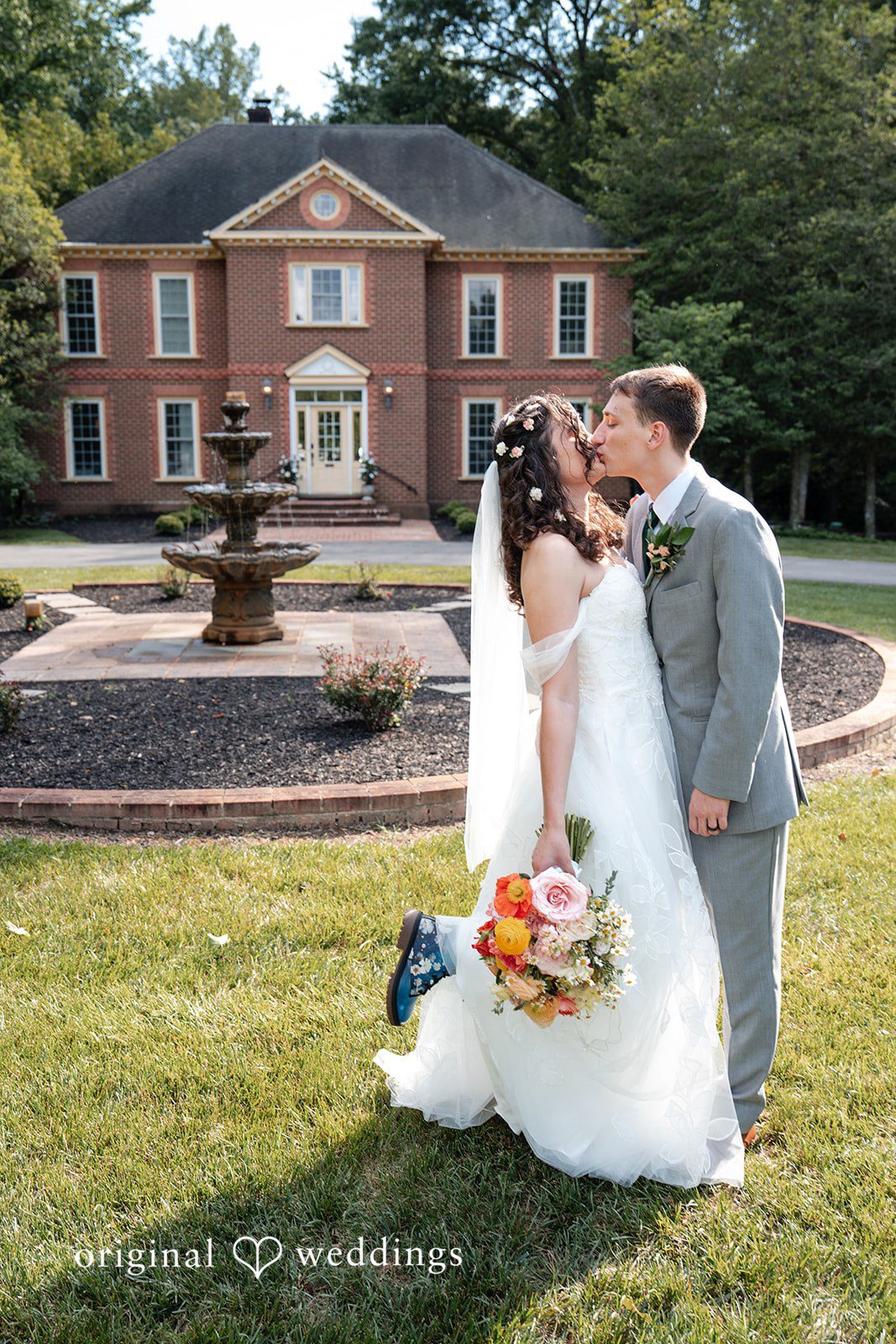 Conner + Ashley A bride and groom kissing in front of a brick building with a fountain.