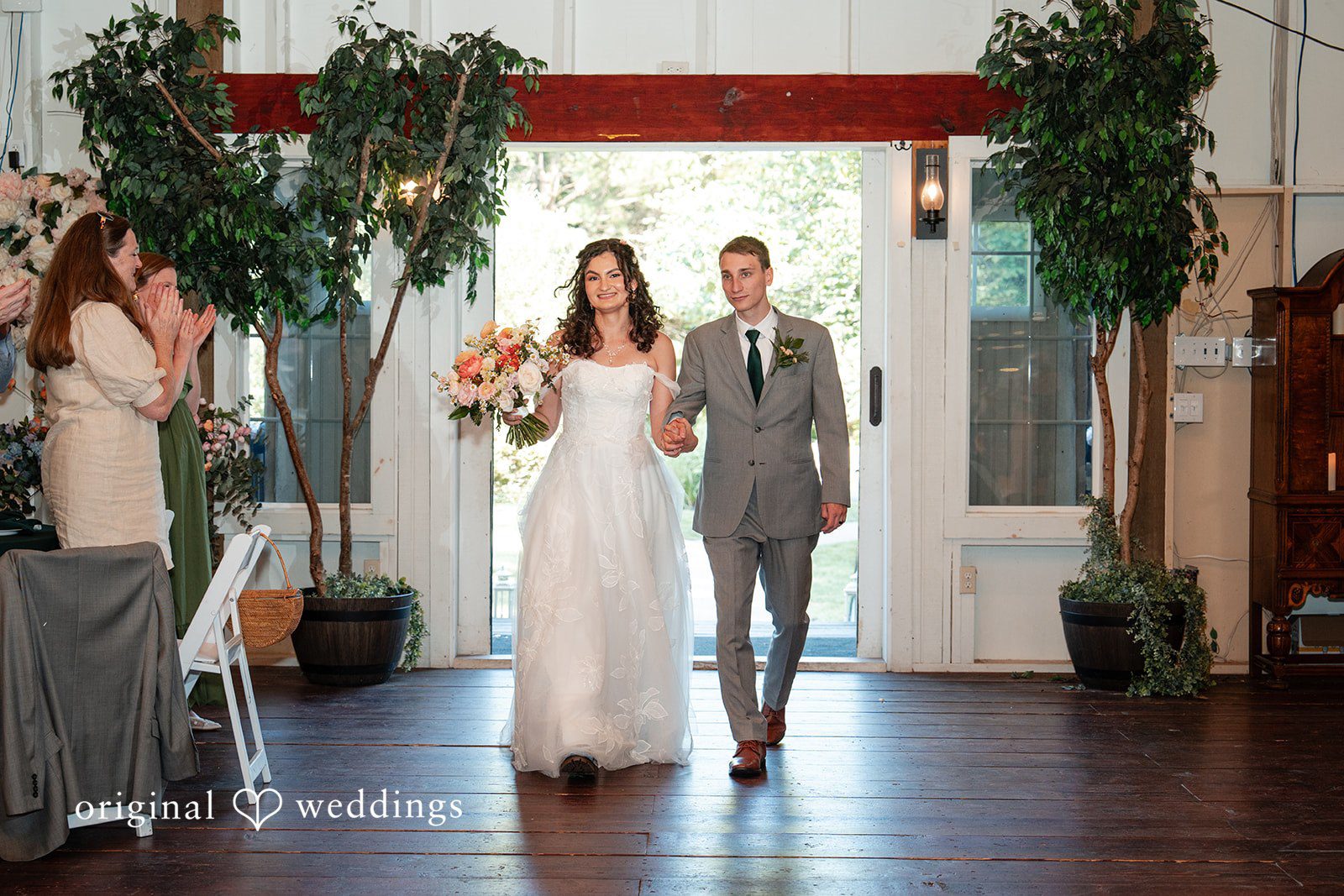 Conner + Ashley A newlywed couple walking hand-in-hand down an aisle into a reception hall.