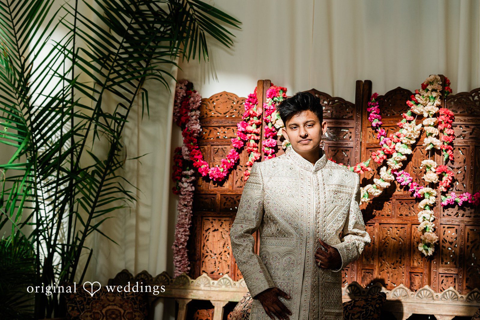 Sonya + Akshaya A groom posing in a traditional sherwani next to a decorative wooden screen.