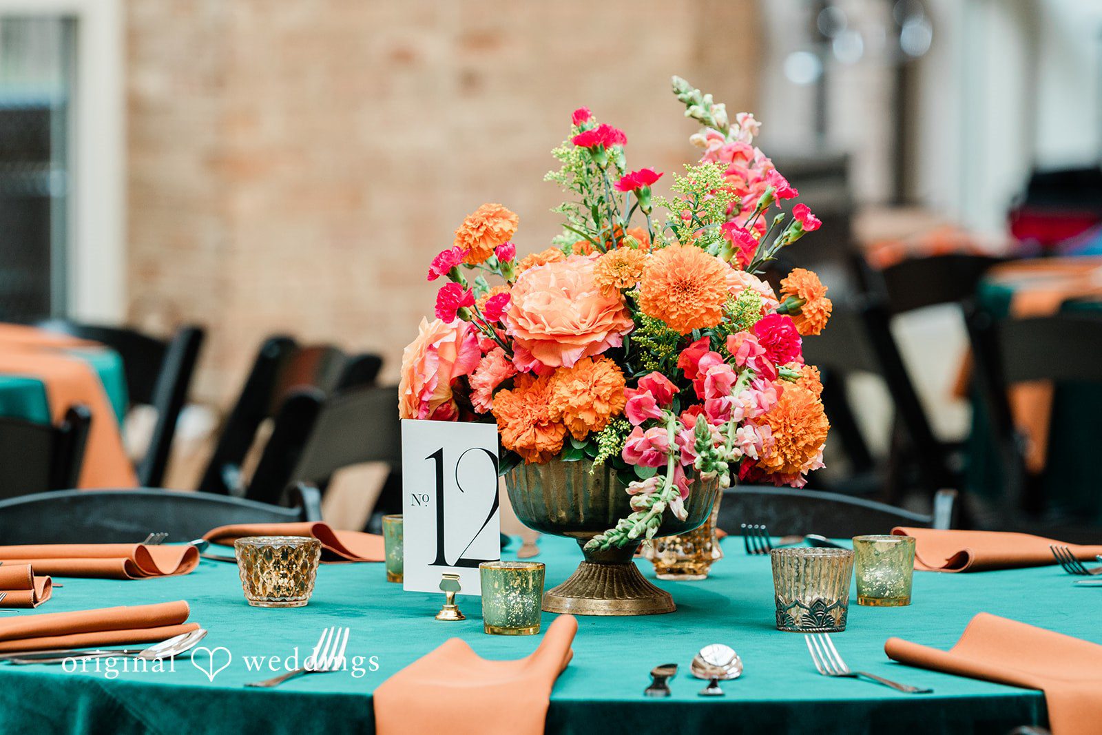 Sonya + Akshaya A close-up of a wedding reception table setting showcasing a vibrant orange and pink floral centerpiece.