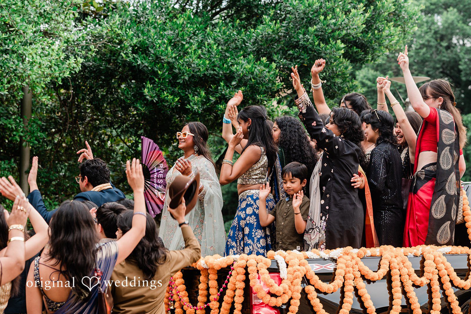 Sonya + Akshaya A energetic crowd of wedding guests with raised hands celebrating near a floral barrier.