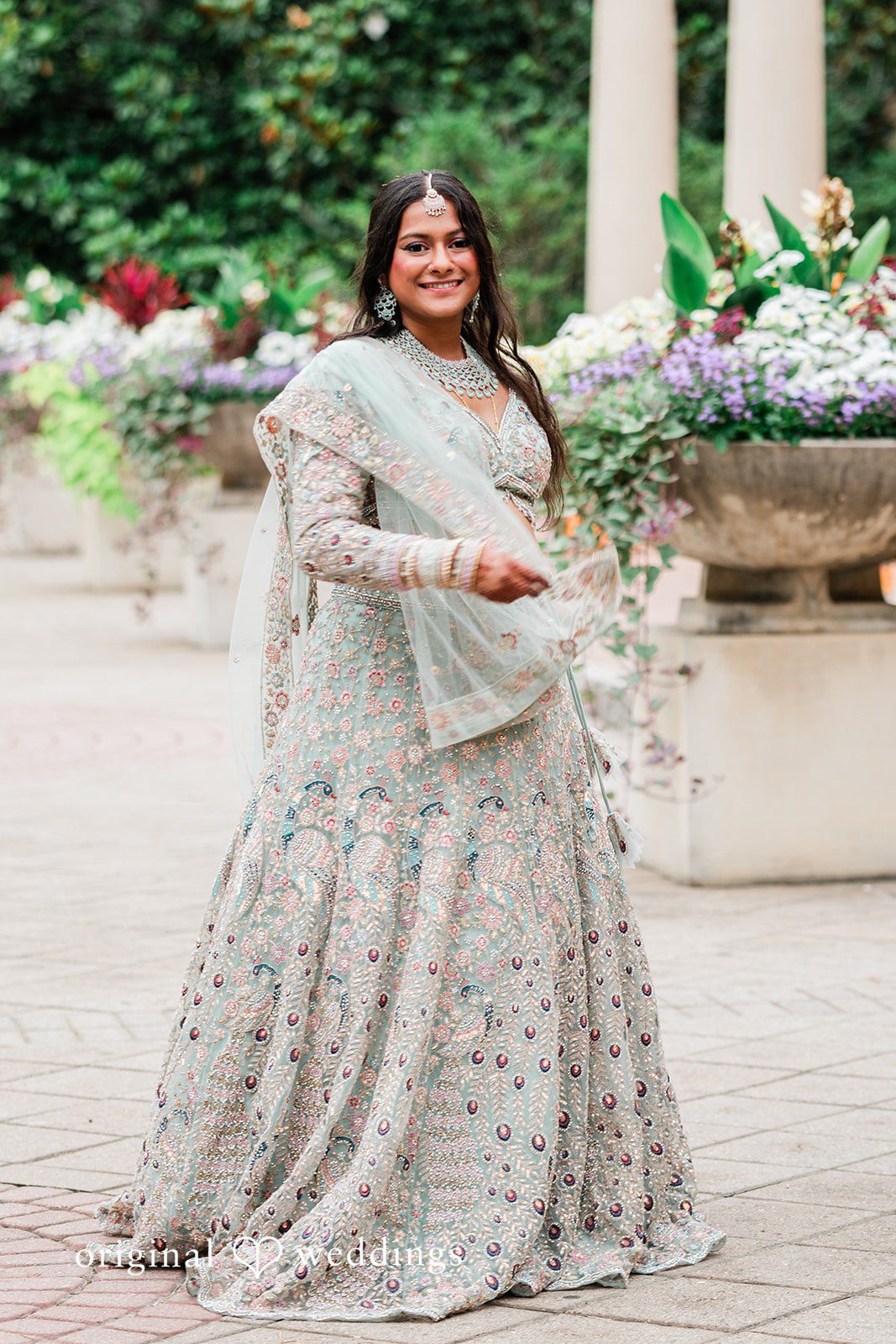 Sonya + Akshaya A full-length portrait of a bride gracefully holding her patterned lehenga.