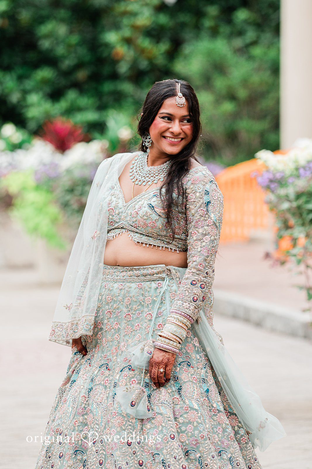 Sonya + Akshaya A smiling bride posing in a heavily embroidered lehenga.