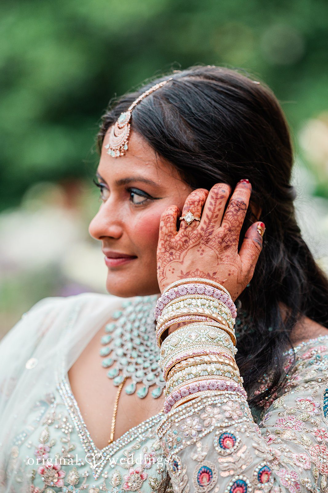 Sonya + Akshaya A close-up portrait of a bride looking to the side while touching her hairs.