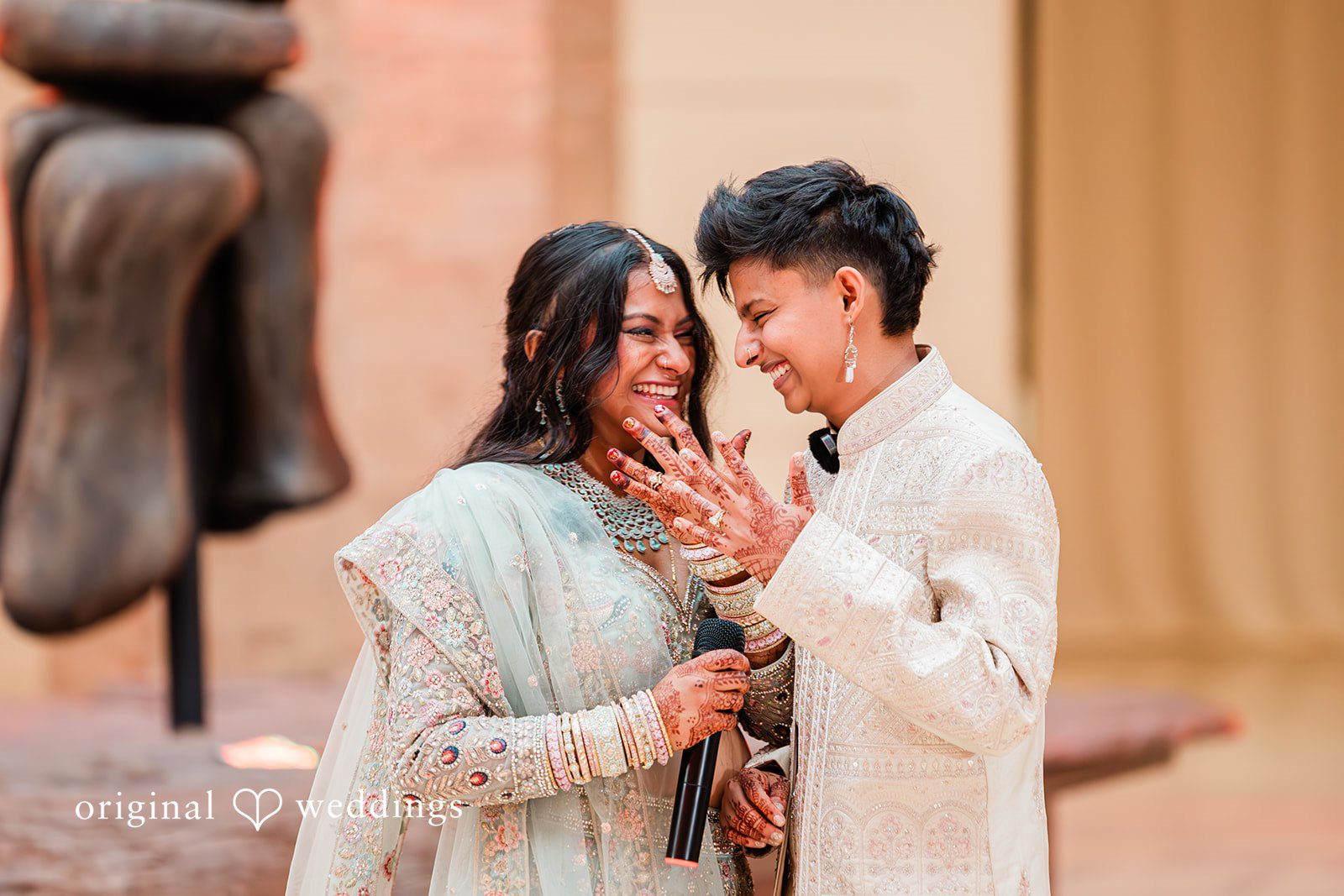 Sonya + Akshaya A bride and groom laughing together and showing rings while looking directly at each other.
