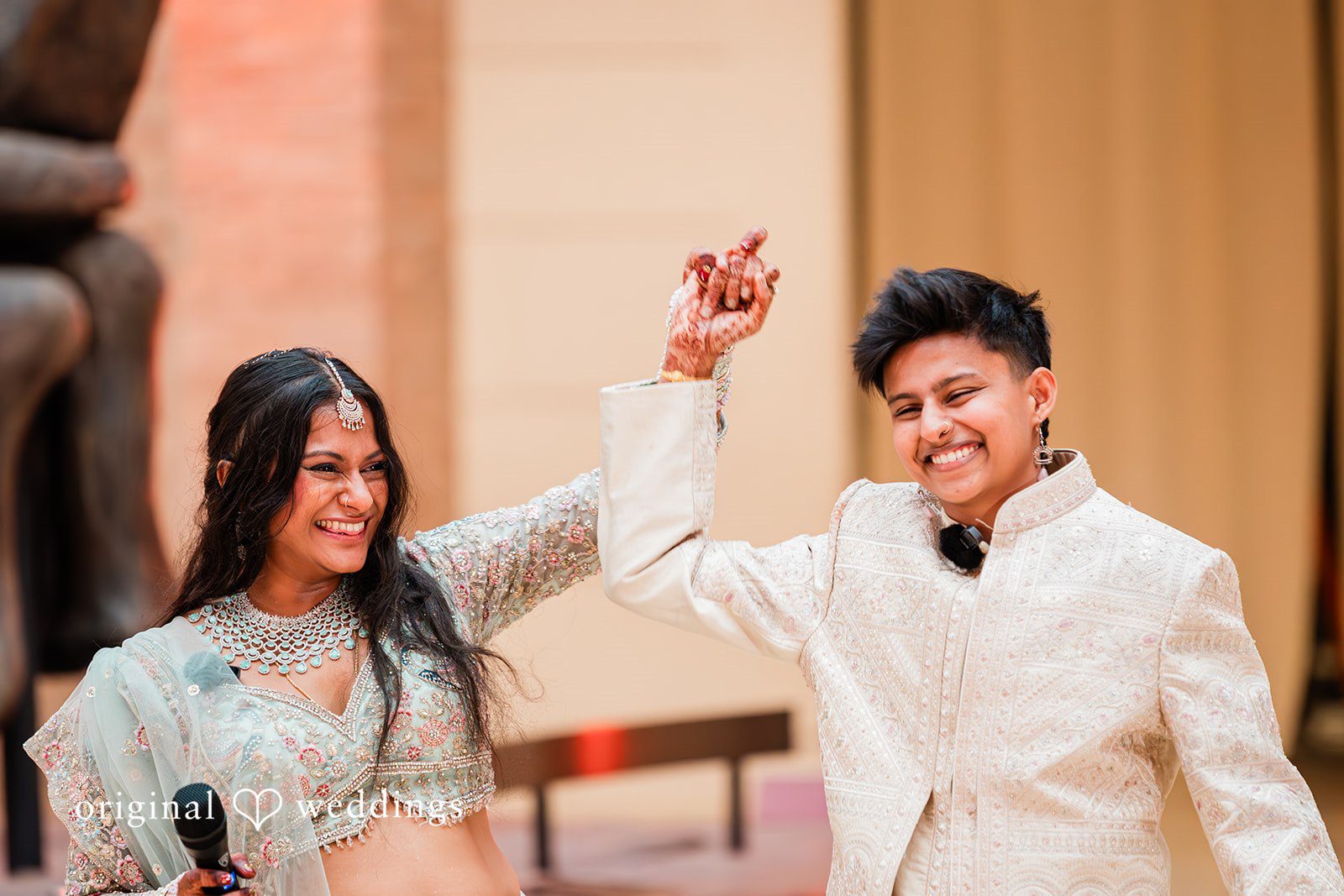 Sonya + Akshaya A joyful couple raising their arms in celebration during their wedding ceremony.