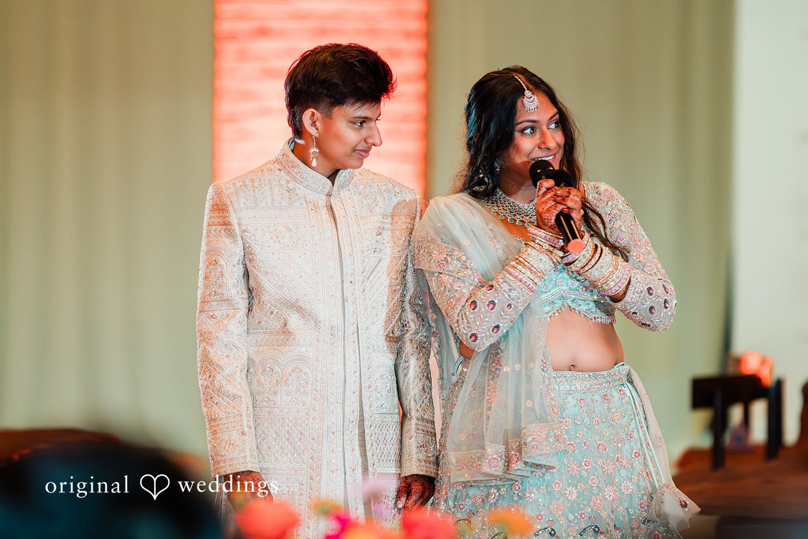 Sonya + Akshaya A bride speaks into a microphone while the groom stands beside her during reception speeches.