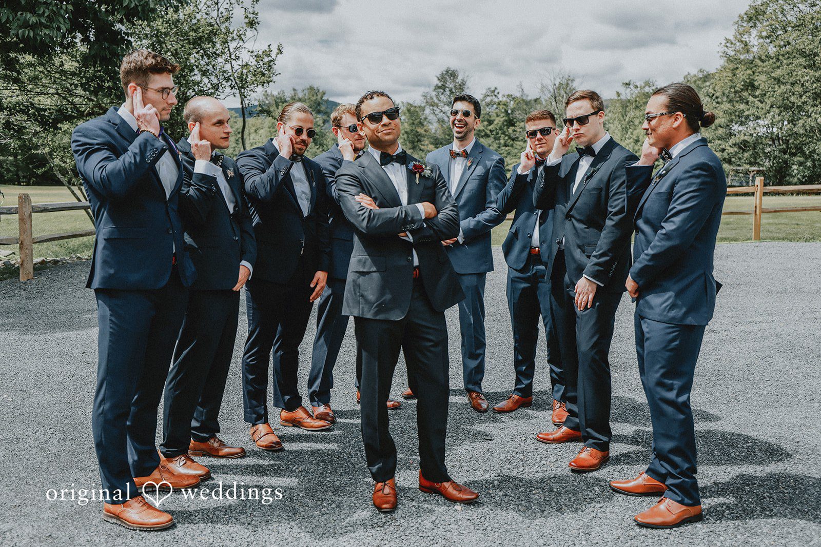 Groomsmen in dark suits standing together and laughing in front of a wooden fence.