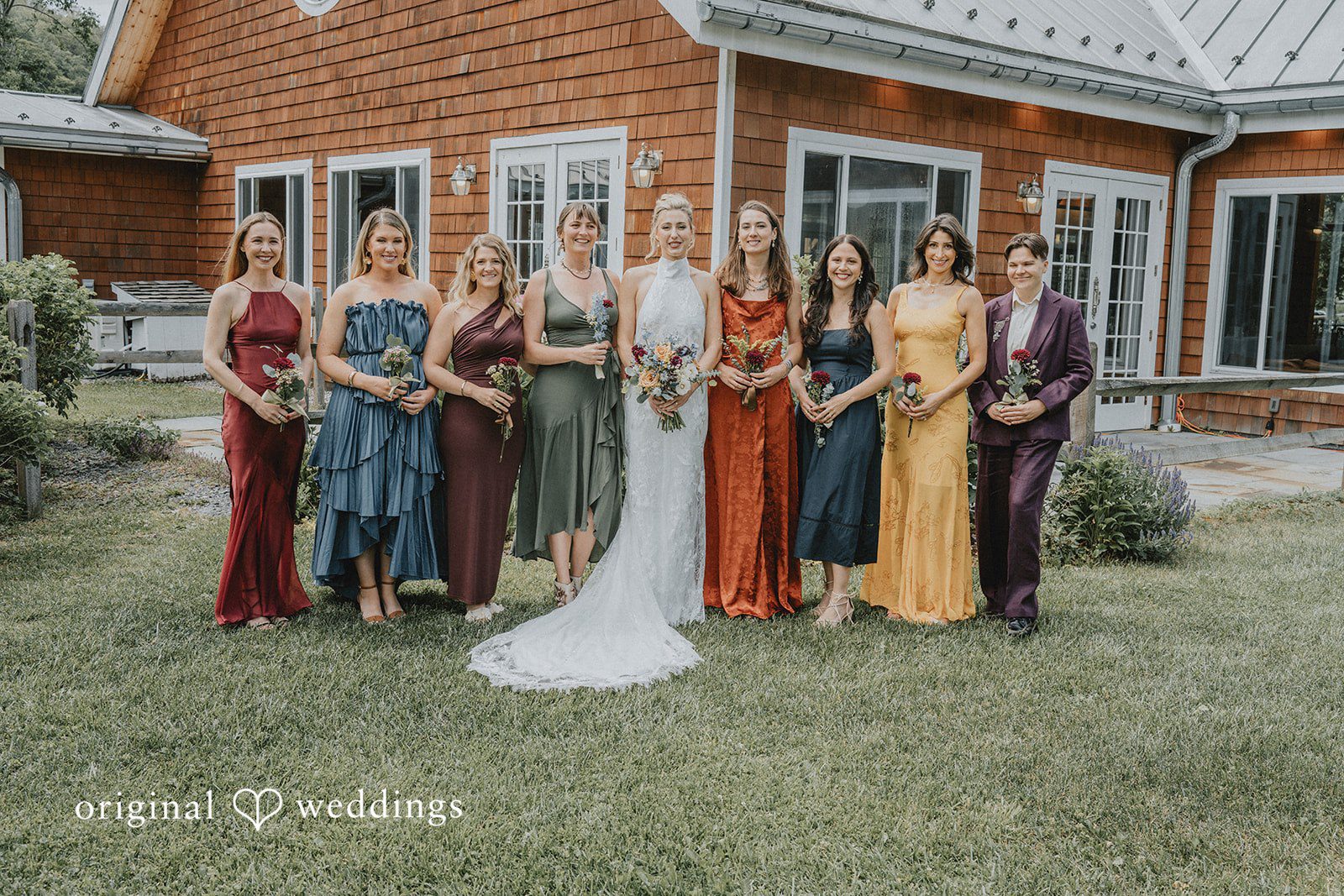Bridesmaids wearing assorted jewel-toned dresses posing together on a lawn.