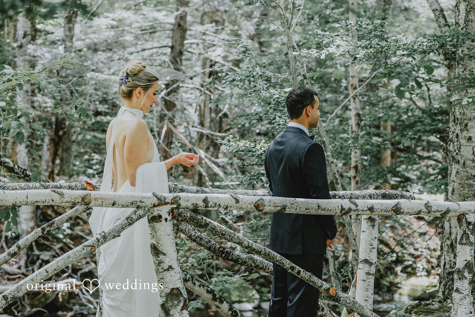Bride and groom walking side by side down a wooden walkway into the woods.