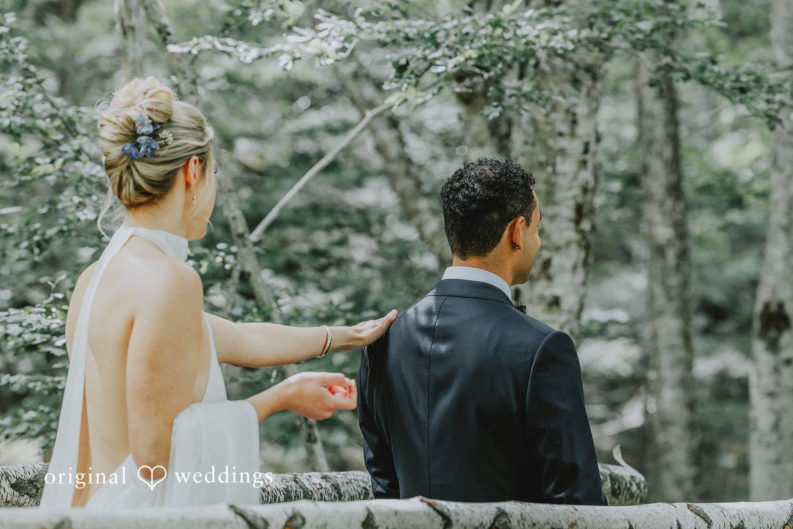 Bride smiling and holding the groom's hand along a rustic wooden fence in the woods.