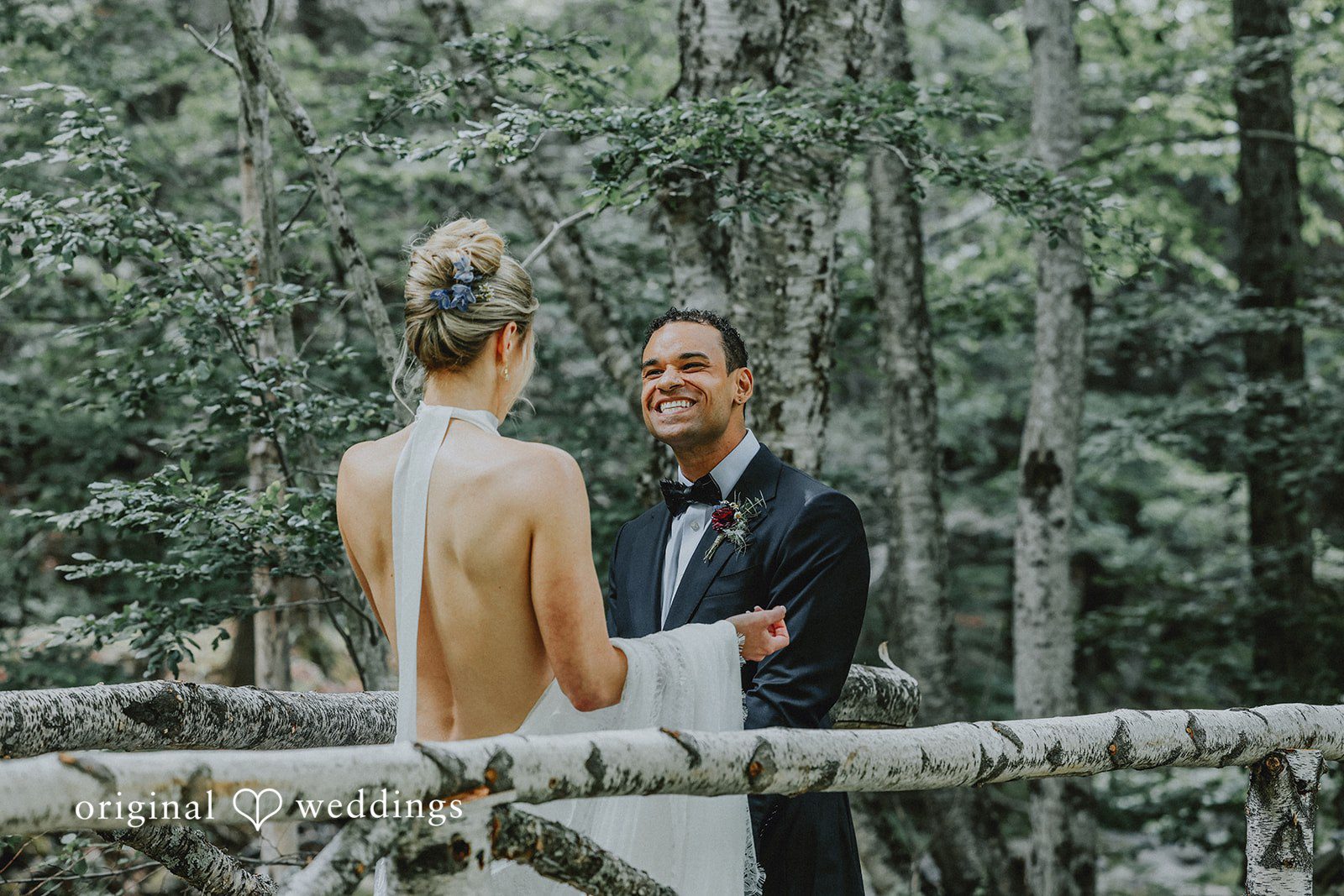 Bride and groom smiling at each other while holding hands in a wooded area.