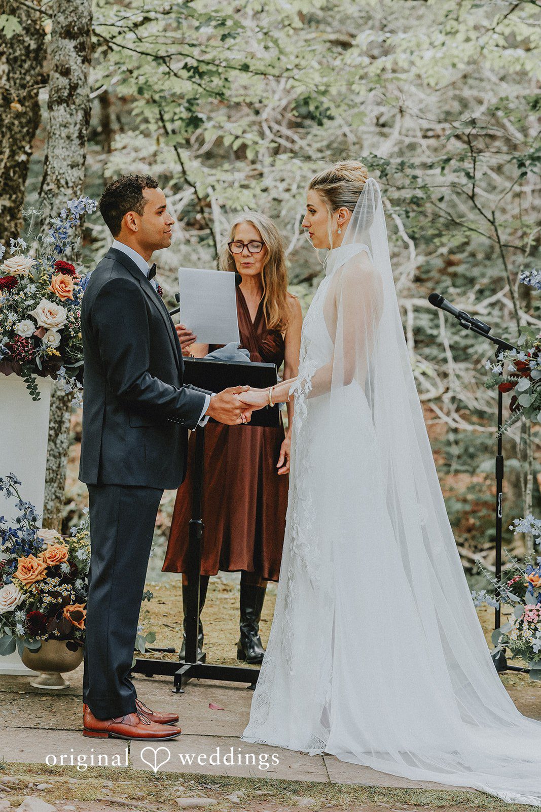 Bride and groom exchanging vows in front of a stone wall backdrop.