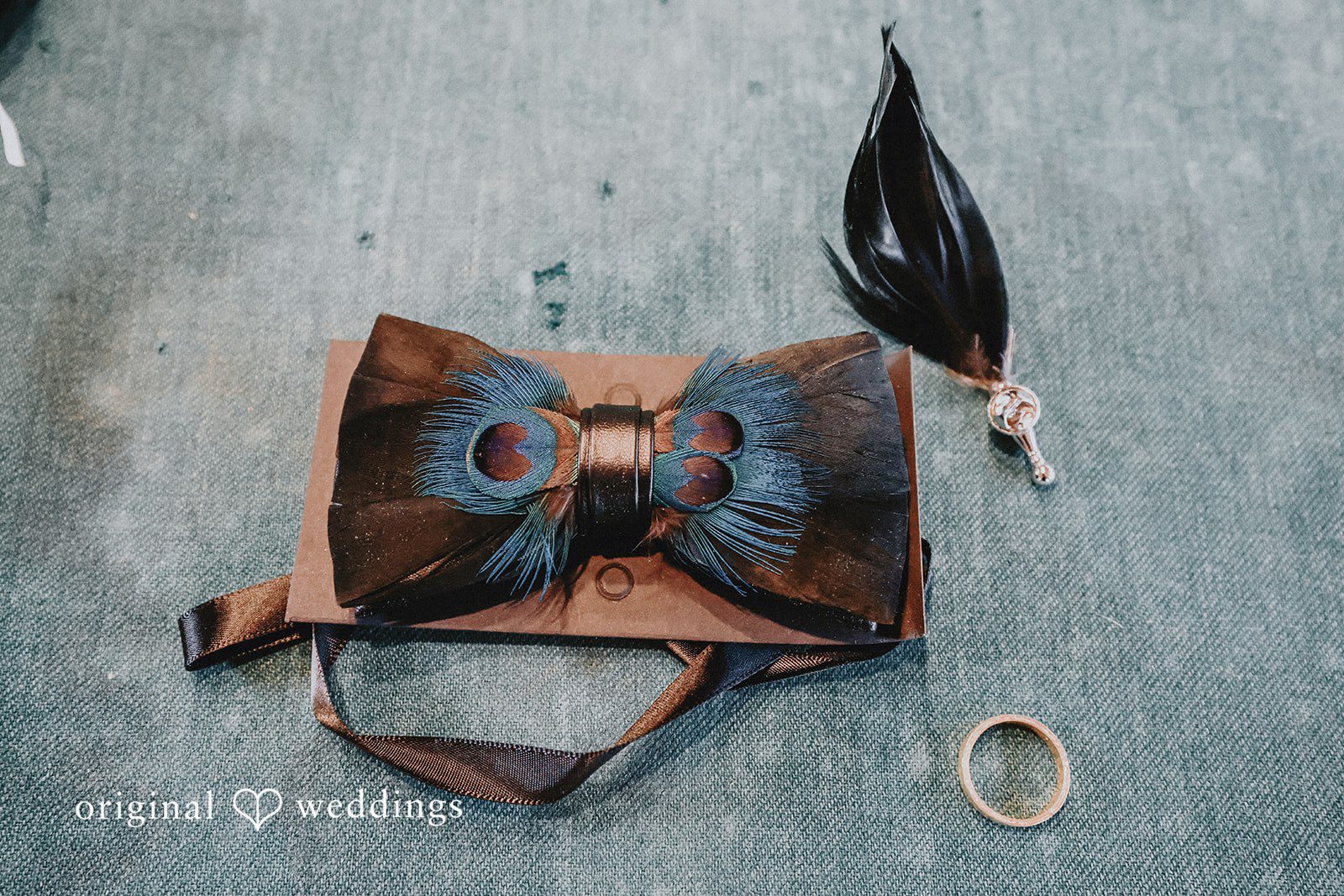 Groom's accessories including a patterned bow tie, leather suspenders, and a feather boutonniere.