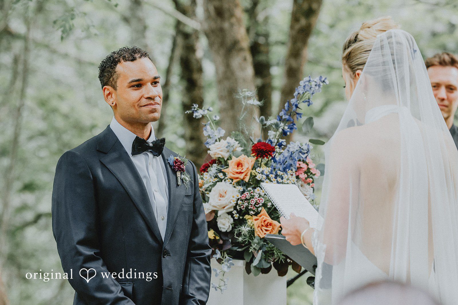 Groom looking at the bride while she reads her wedding vows.