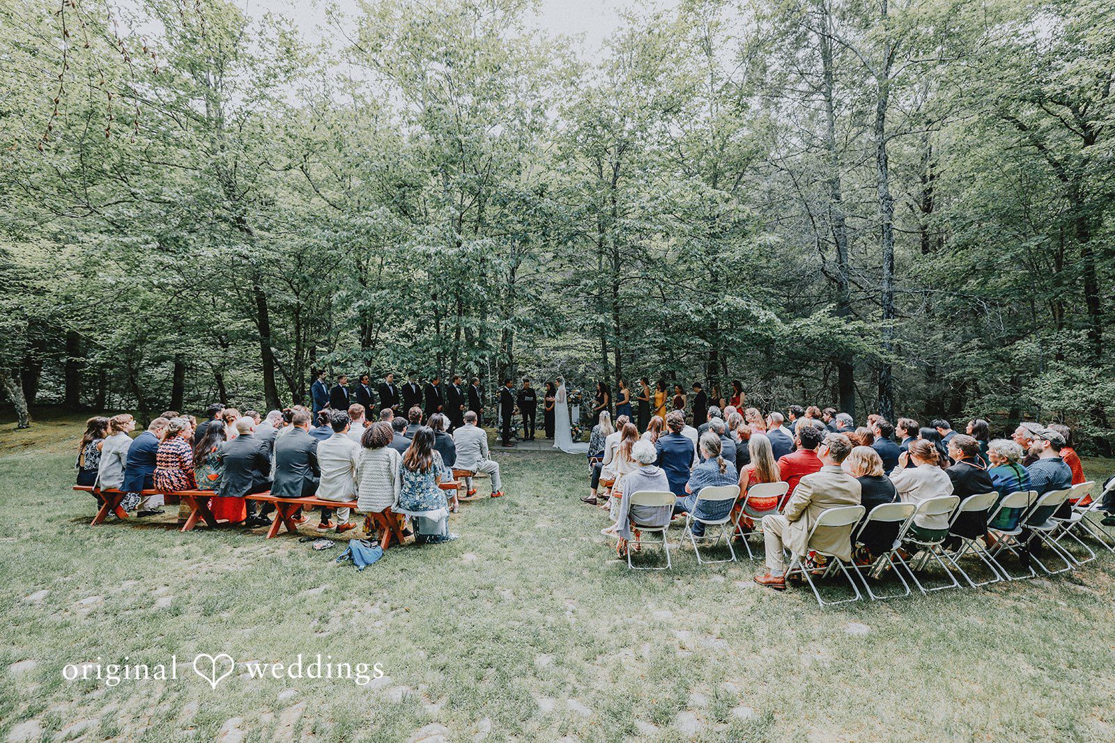 Wide overhead view of an open-air wedding ceremony with guests seated in a wooded clearing.