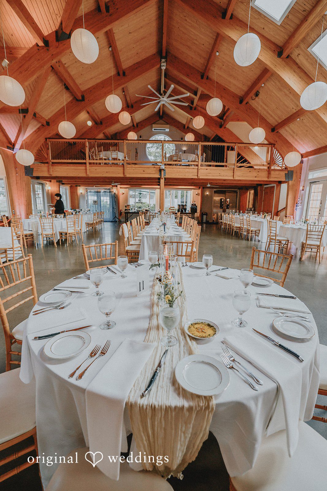 Wide view of an empty reception hall with wooden beams and set tables.