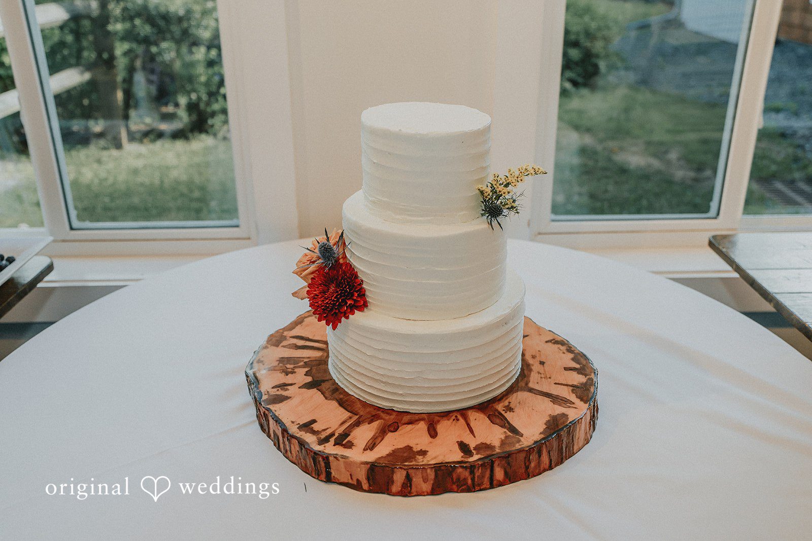 Three-tiered white wedding cake decorated with flowers on a wooden slab.