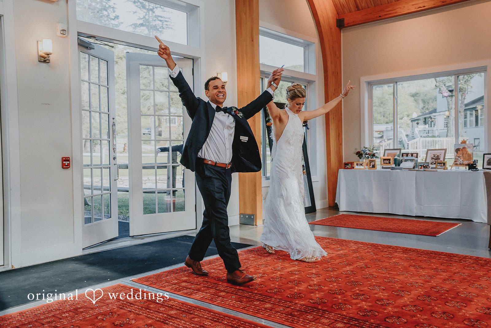 Newlyweds celebrating with raised arms on a red carpet path.