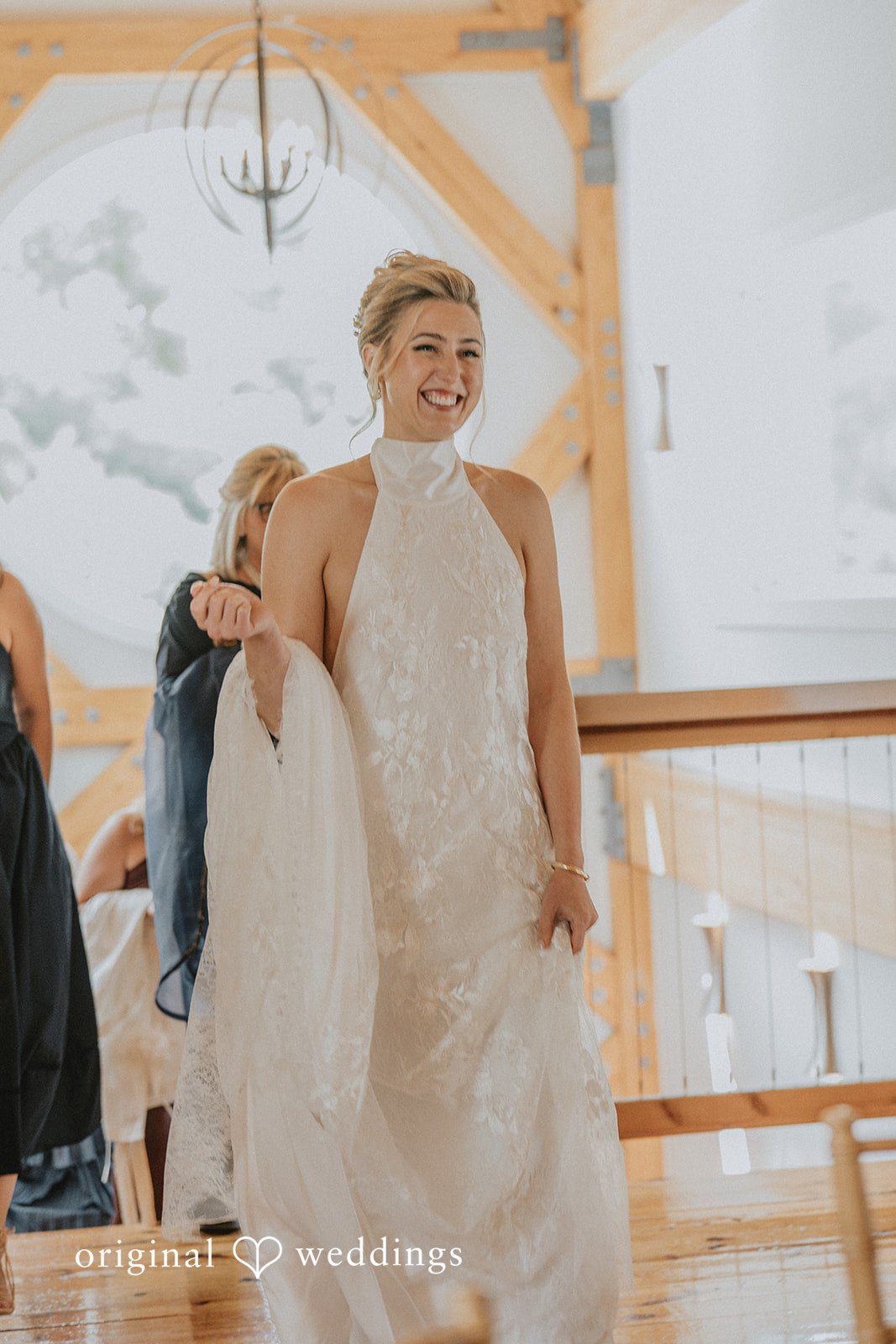 Full-length view of a bride smiling in her wedding gown near a wooden railing.
