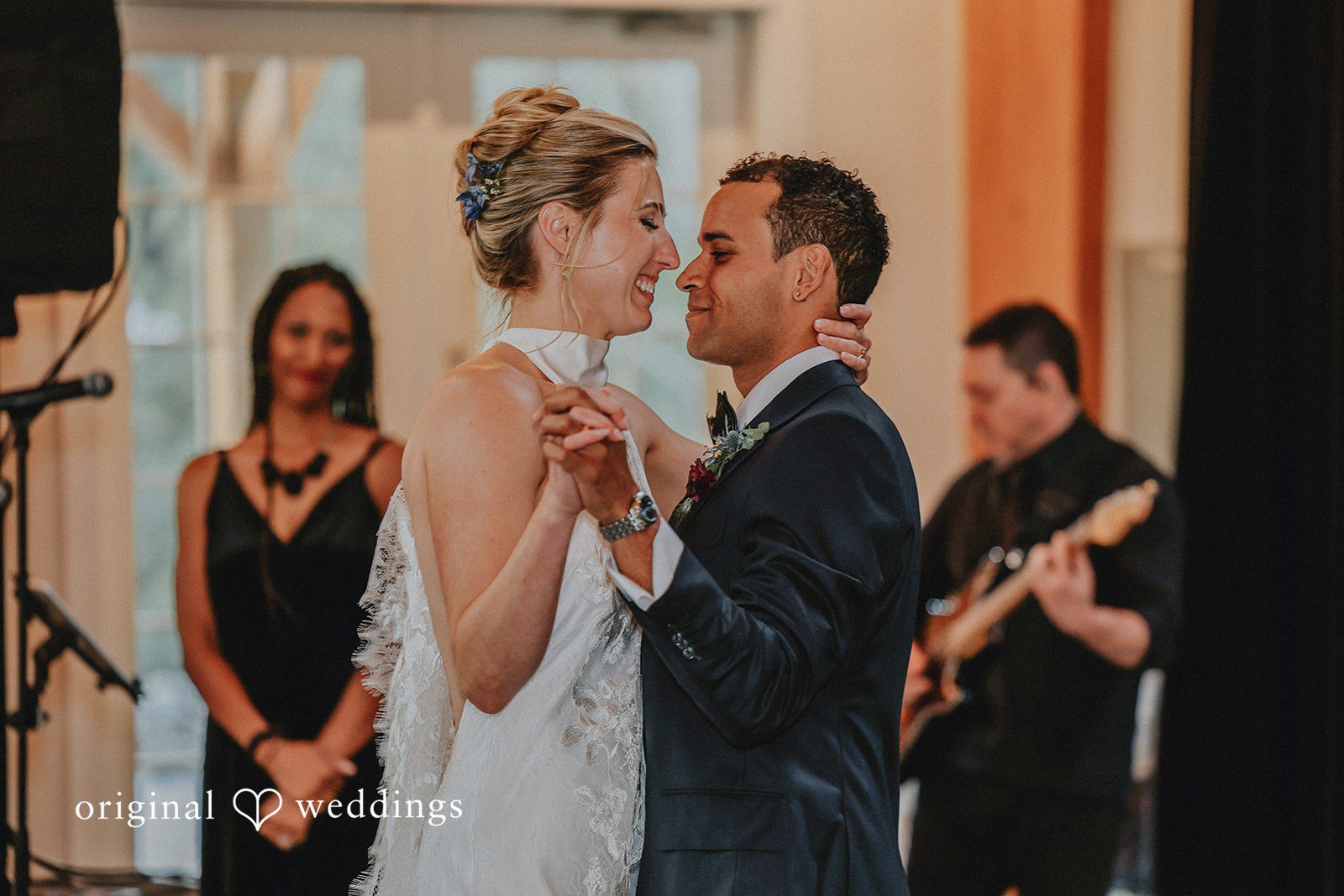Bride and groom smiling and sharing their first dance as guests look on.