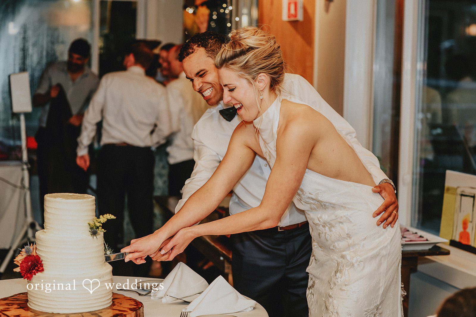 Bride and groom standing together to cut their white tiered wedding cake.
