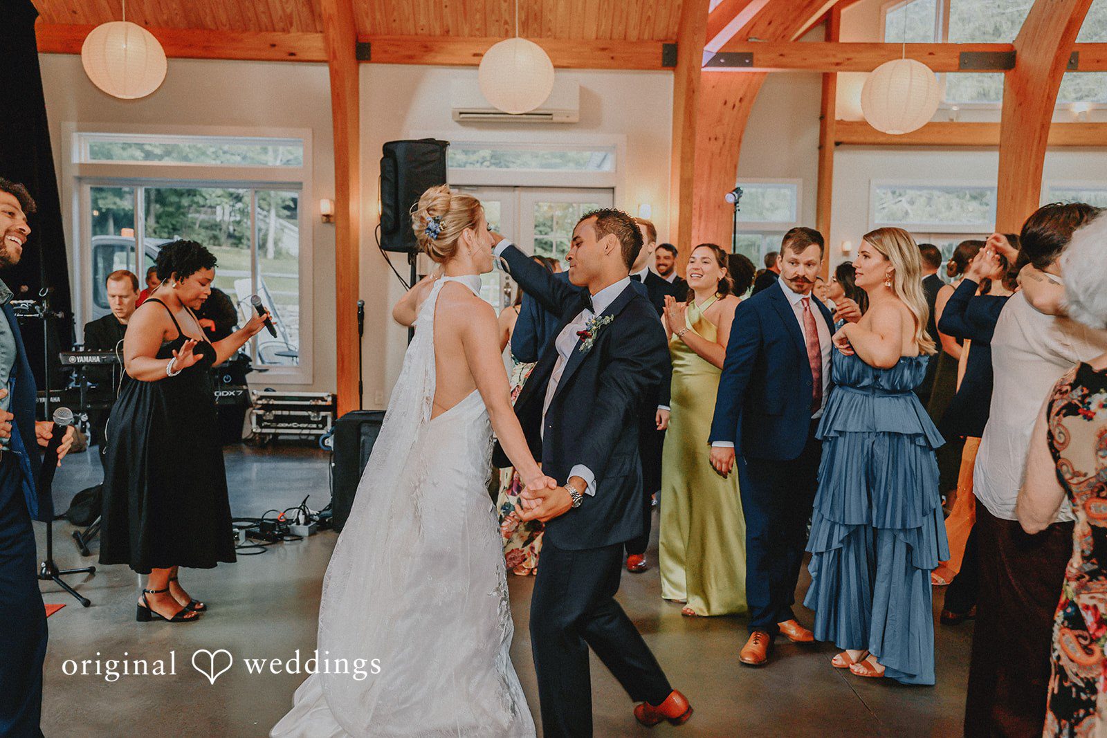 Bride and groom holding hands and talking with guests in a crowded venue.