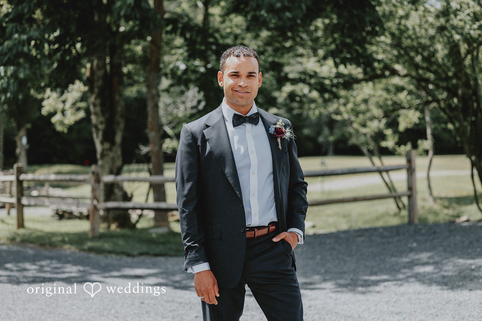 Full-length portrait of a groom posing on a dirt path with trees behind him.