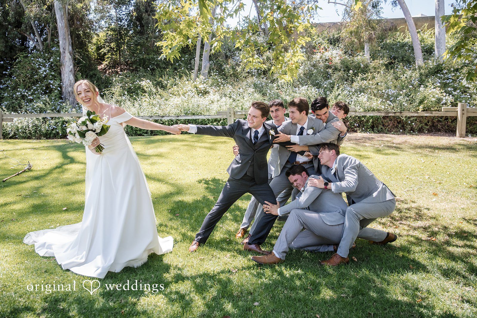 Madeline + Brady Bride laughing while playfully pulling the groom away as the groomsmen hold onto him during wedding picture