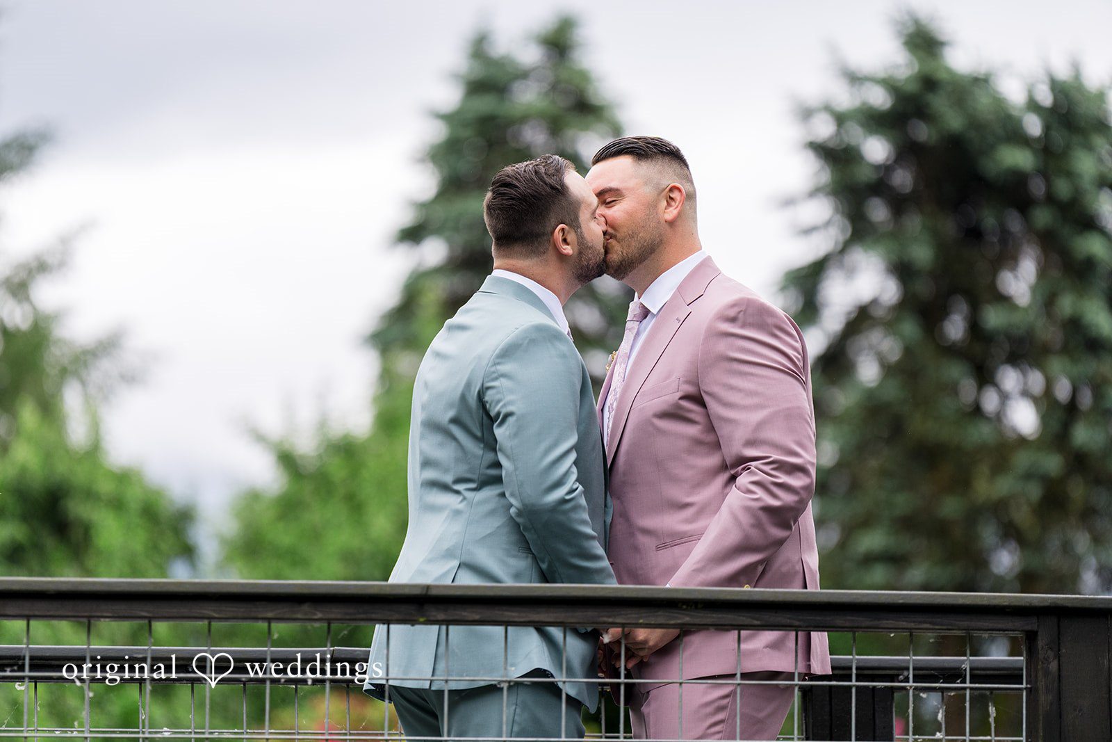 Kristian + Jeff Couple sharing a kiss while standing on a bridge walkway.