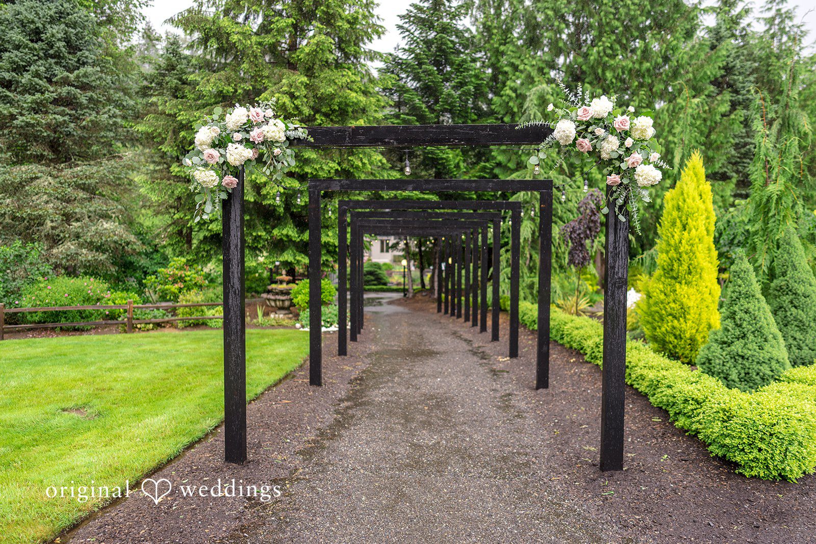 Kristian + Jeff A stone pathway lined with black metal archways and decorative street lamps, bordered by green grass.