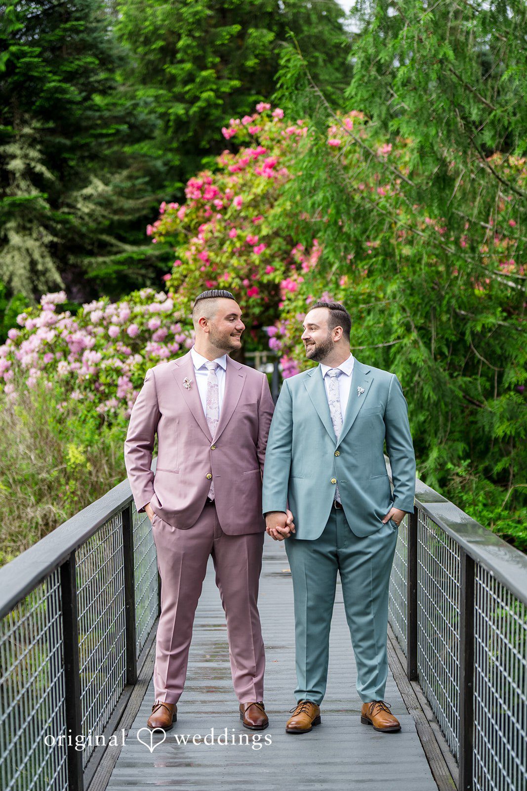Kristian + Jeff Couple standing side-by-side on a bridge walkway and smiling at each other.