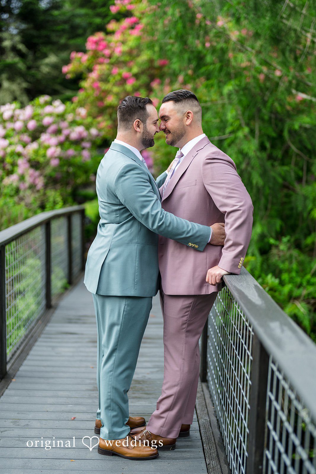 Kristian + Jeff One groom leaning back playfully while hugging the other groom on a bridge walkway.