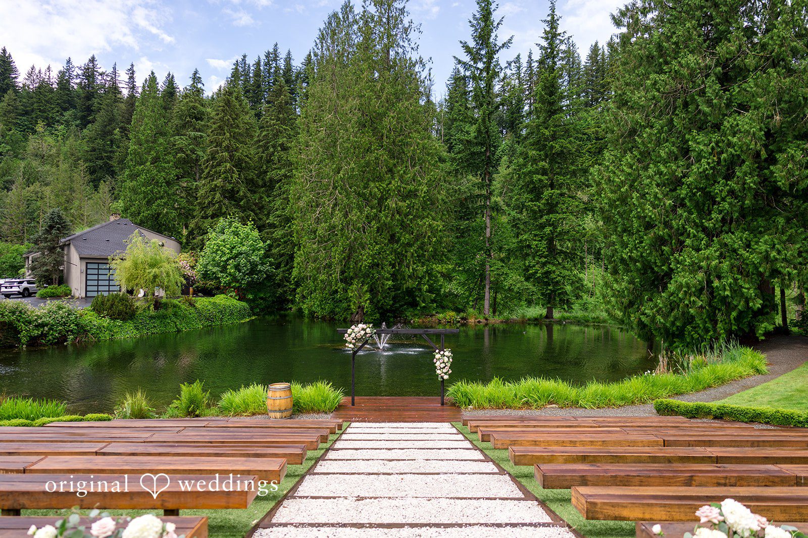 Kristian + Jeff Wooden steps leading down a pathway toward a scenic pond surrounded by a dense green forest.