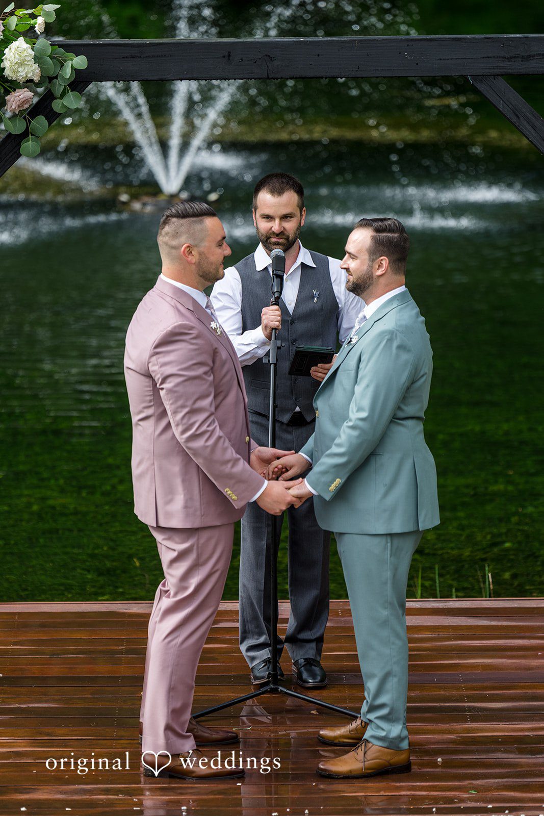 Kristian + Jeff Couple one in a mauve suit and one in a light blue suit, holding hands during their ceremony.